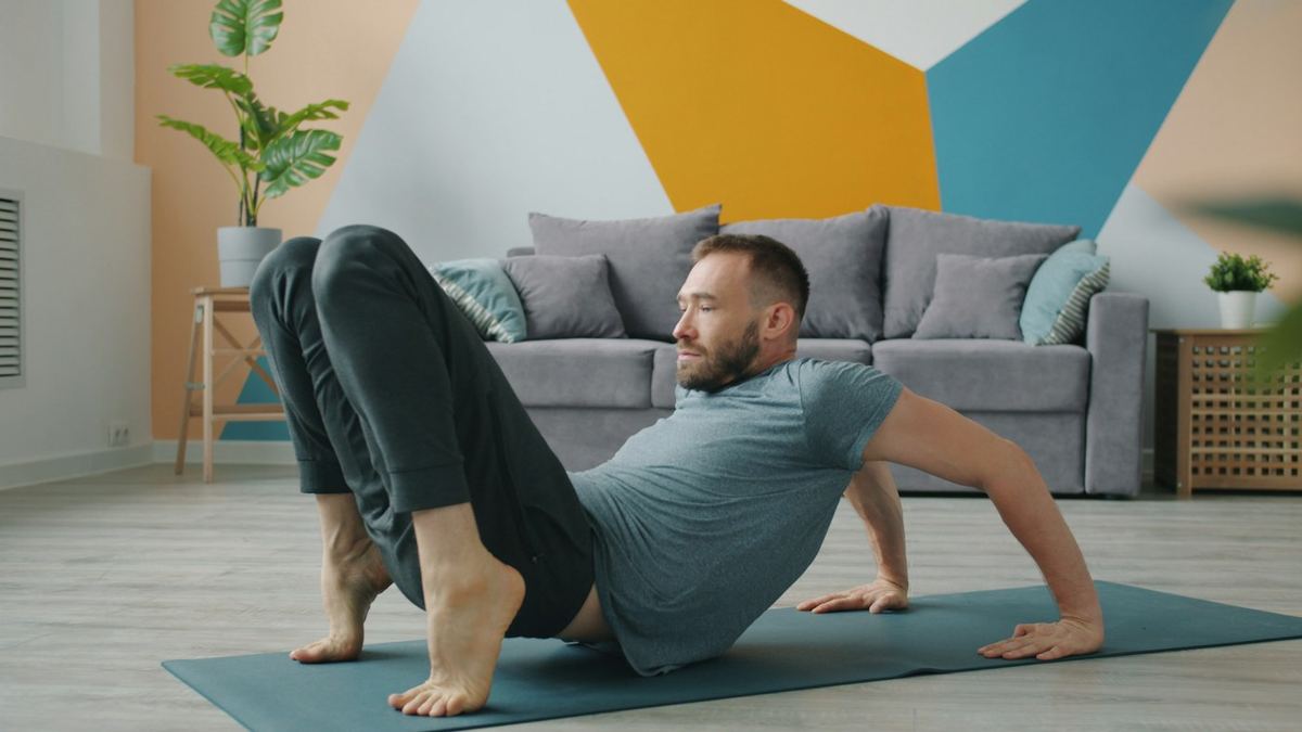 Man på yogamatta i vardagsrummet med böjda knän, i startläge för bäckenlyft